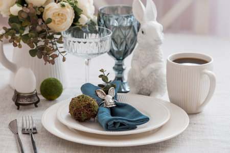 Beautiful spring table setting. A plate with a cotton napkin with a bunny. Silverware and a vase of...