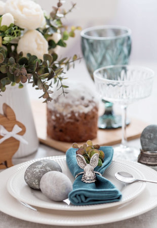 Spring table setting. A plate with a cotton napkin with a bunny, a cake and Easter eggs. Silverware,...