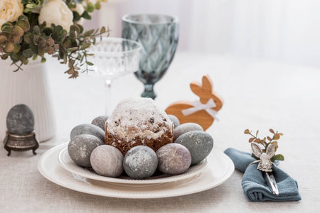Spring table setting. A plate with a cotton napkin with a bunny, a cake and Easter eggs. Silverware,...