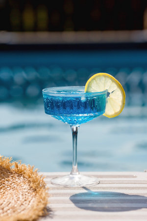 A glass of delicious blue cocktail Blue  and yellow lemons on the background of the pool. Alcoholic cocktail juicy fruit blue with curacao liqueur, ice cubes and a slice of lemon.の写真素材