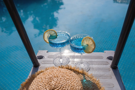 A glass of delicious blue cocktail Blue Lagoon and yellow lemons on the background of the pool. Alcoholic cocktail juicy fruit blue with curacao liqueur, ice cubes and a slice of lemon.の写真素材