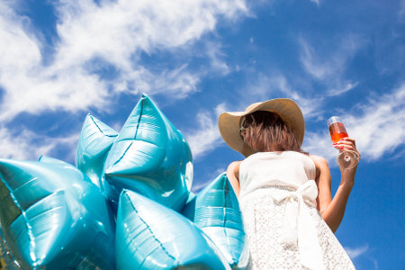 Young girl with silver and blue balloons outdoors. A woman holds balloons at arm's length against a beautiful blue sky. The concept of freedom and celebration.の写真素材