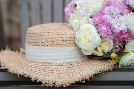 A bouquet of white fluffy peonies, delicate pink carnations and a straw hat. close-up. The concept of summer and recreation.の写真素材