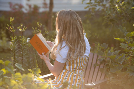 Beautiful blonde woman in a green summer garden on a chaise longue. A girl in a yellow sundress and...