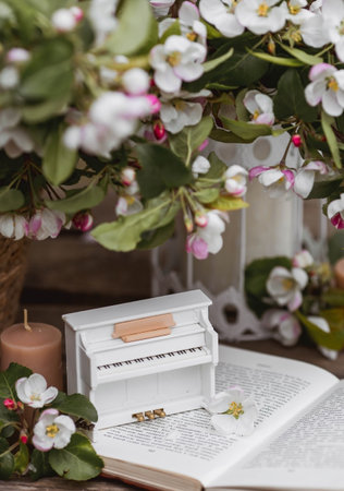 A beautiful postcard. A white piano, a statuette, candles, a book and a vase with a bouquet of blooming apple trees. A beautiful still life. The concept of classical music, poetry.の写真素材