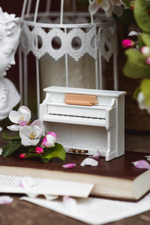 A beautiful postcard. A white piano, a statuette, candles, a book and a vase with a bouquet of blooming apple trees. A beautiful still life. The concept of classical music, poetry.の写真素材