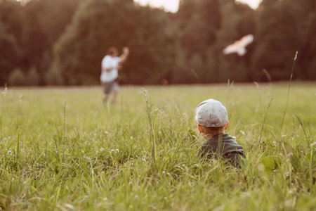 Family vacation. Summer outdoor photo of a father and son flying a kite in a meadow. A picture against the sun. Warm family moments or a conceptual image for spending time outdoors.の写真素材