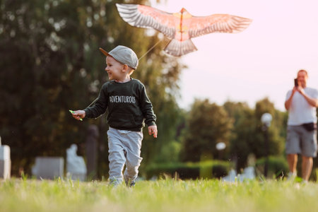 Family vacation. Summer outdoor photo of a father and son flying a kite in a meadow. A picture against the sun. Warm family moments or a conceptual image for spending time outdoors.の写真素材