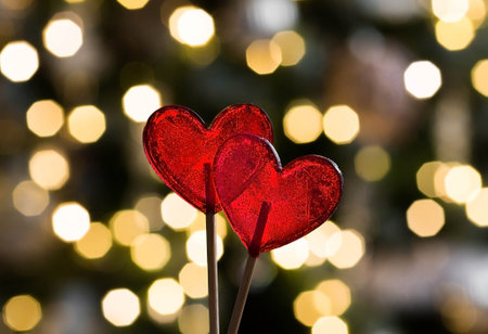 Two lollipops in the shape of red hearts. Candy on a stick on the background of beautiful bokeh. The...