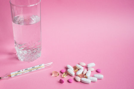 Glass of water, thermometer, pills, medicinMoscow, March 2019es falling out of a white plastic bottle on a pink background.の写真素材