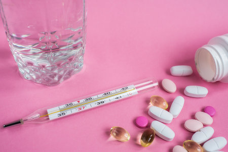 Glass of water, thermometer, pills, medicinMoscow, March 2019es falling out of a white plastic bottle on a pink background.の写真素材