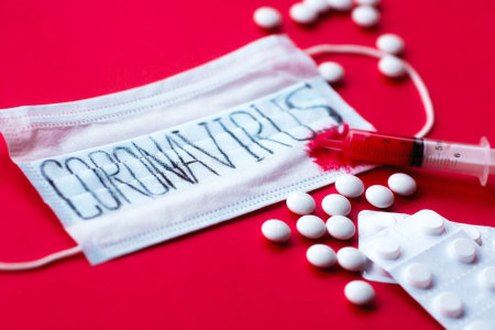 Surgical mask protective mask with text coronavirus, pills and syringe with blood. Chinese coronavirus outbreak. red background. Novel coronavirus - 2019-nCoV, WUHAN virus concept.の写真素材