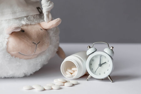 A tube of pills, a sheep in a sleep cap and an alarm clock. The time on the clock is 2 am. Insomnia and recovery of sleep mode. Count sheep to fall asleep.の写真素材