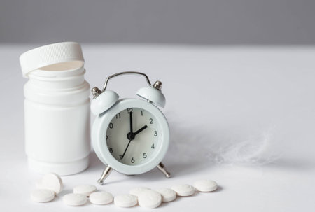 A tube of pills and an alarm clock. The time on the clock is 2 am. Insomnia and recovery of sleep mode. Taking pills by the hour.の写真素材