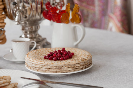 Russian traditions. Russian holiday Maslenitsa. Still life with a cup of tea, a stack of pancakes with northern cranberries, cubes of butter and samovars on the table.の写真素材
