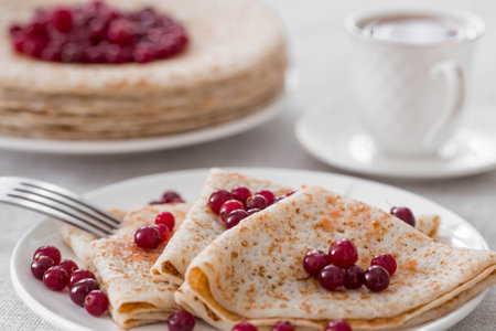 Russian traditions. Russian holiday Maslenitsa. Still life with a cup of tea, a stack of pancakes with northern cranberries, cubes of butter on the table.の写真素材