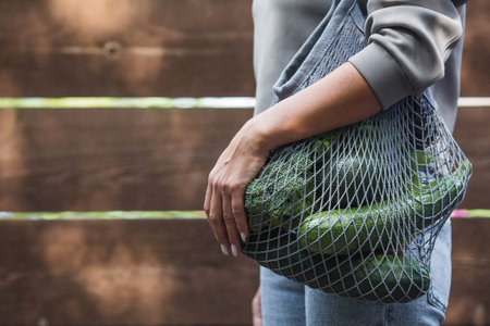 A modern stylish woman with a shopping bag, buying green vegetables against the background of the...