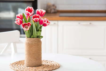 A bouquet of tulips in a vase. In the background is the interior of a white Scandinavian-style kitchen. The concept of home comfort and International Women's Day on March 8.の写真素材