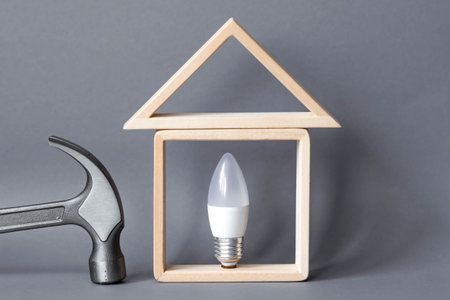 Ideas for home renovation. A model of a wooden house, a light bulb and a hammer on a gray background. The concept of renovation and design of the room.の写真素材