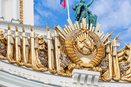 The golden coat of arms of the USSR on Pavilion No. 1 "Central" against a bright blue sky. Close-up. VDNH. Moscow. Russiaのeditorial素材