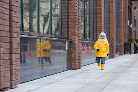 Portrait of a small child 4 years old in yellow rubber boots and a jacket. The kid walks in the park in the spring. Photo of spring and autumn holidays.の写真素材