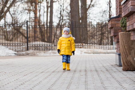Portrait of a small child 4 years old in yellow rubber boots and a jacket. The kid walks in the park in the spring. Photo of spring and autumn holidays.の写真素材