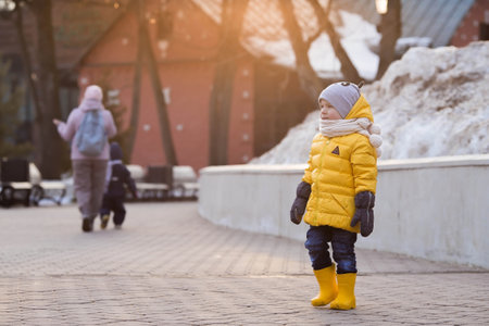 Portrait of a small child 4 years old in yellow rubber boots and a jacket. The kid walks in the park in the spring. Photo of spring and autumn holidays.の写真素材