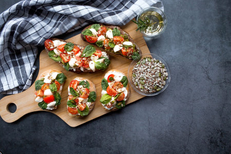 Bruschetta (sandwiches) with cherry tomatoes, mozzarella cheese and herbs on a cutting board on a dark background. Traditional Italian snack.の写真素材