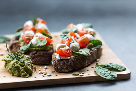 Bruschetta (sandwiches) with cherry tomatoes, mozzarella cheese and herbs on a cutting board on a dark background. Traditional Italian snack.の写真素材