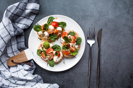Bruschetta (sandwiches) with cherry tomatoes, mozzarella cheese and herbs on a stylish plate on a dark background. A traditional Italian snack.の写真素材