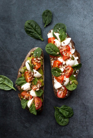 Bruschetta (sandwiches) with cherry tomatoes, mozzarella cheese and herbs on a dark background. A traditional Italian snack.の写真素材