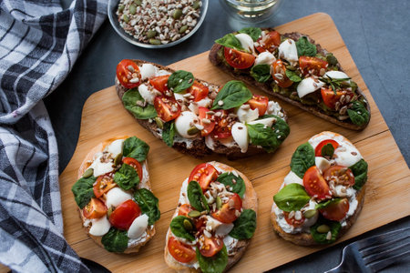 Bruschetta (sandwiches) with cherry tomatoes, mozzarella cheese and herbs on a cutting board on a dark background. Traditional Italian snack.の写真素材