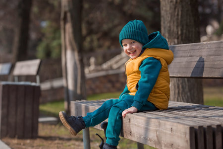A little boy walks in the spring on the playground. A child is sitting on a bench in the fresh air on a sunny spring day. Childhood and child development.の写真素材