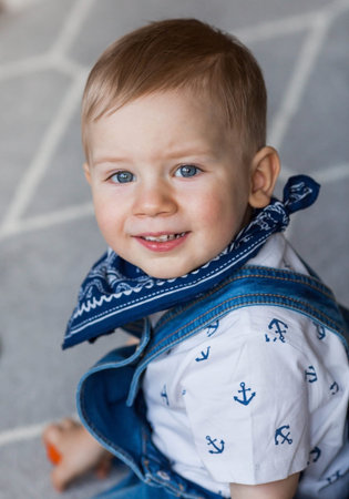 Portrait of a two-year-old boy in a denim jumpsuit with big blue eyes. Childhood.