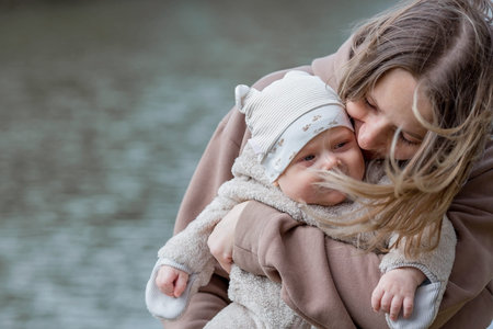 A young mother holds a charming little son in her arms. The kid looks at the camera and smiles....