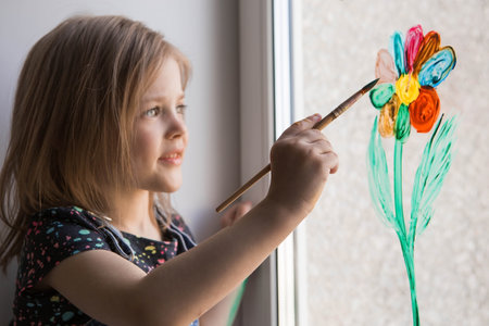 Art and creativity. A happy little girl of 4 years old draws flowers in the window. Children's games for child development. springtime.の写真素材