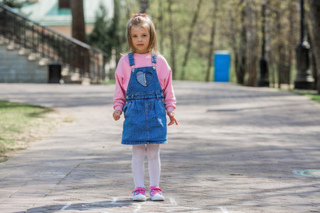 A happy girl in pink clothes draws classics with chalk on the asphalt on the street. Portrait of a...