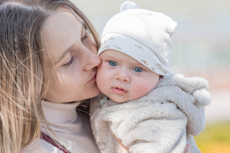 A young mother holds a charming little son in her arms. The kid looks at the camera and smiles. Portrait of a beautiful chubby 4-month-old baby.の写真素材
