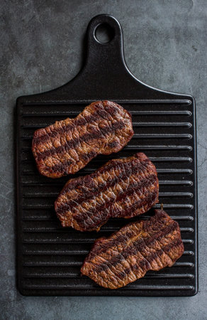 fresh meat. Grilled beef steaks on a stylish board on a dark background. flat top view.の写真素材