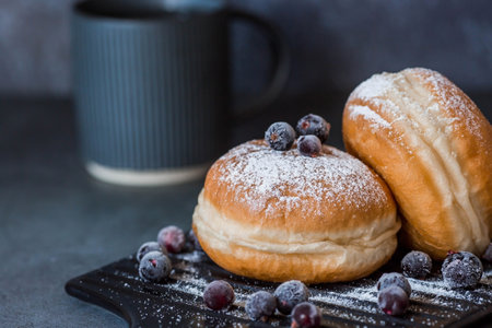Delicious dessert. A donut with berry filling, fresh currant berries, powdered sugar and a cup of black coffee or tea on a dark background. sweets.の写真素材