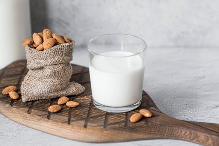 Organic almond milk in a glass bottle next to an almond in a bag on a stylish wooden board on a stone table. Natural eco-friendly products.の写真素材
