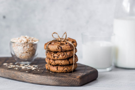 Organic natural cow's milk in a glass bottle, oatmeal and oatmeal cookies on a stylish wooden board on a stone table. Natural eco-friendly products.の写真素材