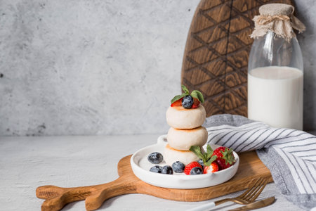 Cottage cheese pancakes, Russian cheesecakes with fresh blueberries, strawberries and mint on a stylish wooden board on a gray concrete table. natural products. Healthy and delicious breakfast.の写真素材