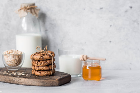 Organic natural cow's milk in a glass bottle, oatmeal, honey and oatmeal cookies on a stylish wooden board on a stone table. Natural eco-friendly products.の写真素材