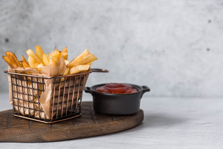 French fries in a metal basket with salt and ketchup on a stylish board on a concrete kitchen table....
