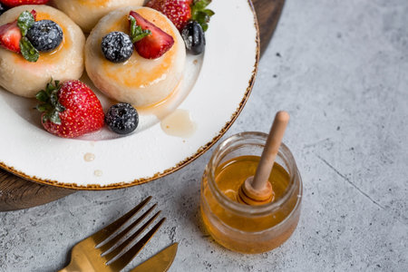 Cottage cheese pancakes, Russian cheesecakes with fresh blueberries, strawberries, honey and mint leaves on a stylish wooden board on a gray concrete table. natural products. Healthy and delicious breakfast.の写真素材