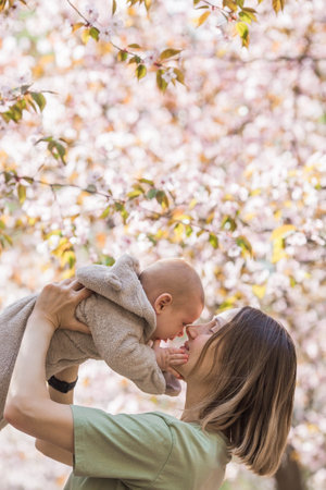 A charming boy in nature among flowering trees in his mother's arms. A child of 4 months plays with his mother and smiles. Family, pregnancy and childbirth.の写真素材