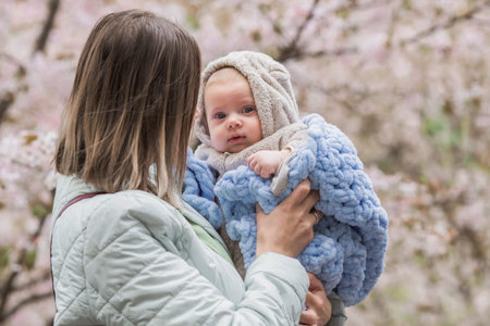 A charming boy in nature among flowering trees in his mother's arms. A child of 4 months plays with...