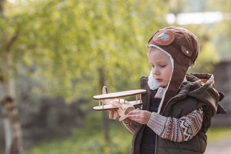 A little boy of 4 years old in an aviator's hat plays with a wooden airplane outdoors in spring. Children's wooden toys for child development.の写真素材