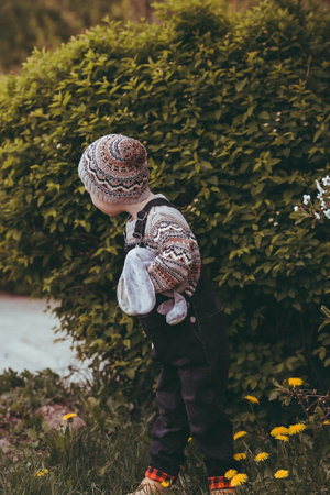 A little boy of 4 years old in stylish clothes outdoors playing with a stuffed rabbit. A beautiful portrait of a child playing on the street. happy childhood.の写真素材